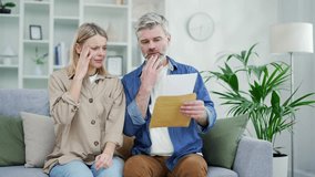 Unhappy married couple received a letter with bad news while sitting on the sofa at home. Mature sad husband and wife open letter and read unpleasant notification about financial debt, have bad mood - Powered by Shutterstock - Get 15% off with code: PIKWIZARD15