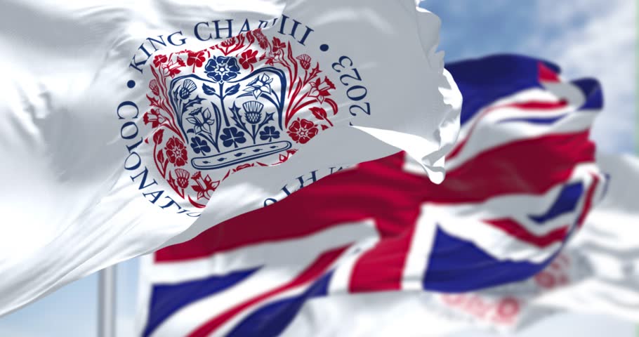 London, UK, April 2023: Flags with the emblem of the coronation of King Charles III and of UK waving. 3d render animation. Slow motion. Seamless loop. Selective focus. Close-up. Fluttering textile