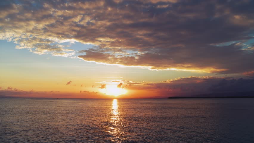 Orange sunset over the sea on a summer tropical evening. Sea waves with a reflection of the setting sun. Ripples of water with sunbeams. Blue ocean under orange skies. Twilight over the sea.