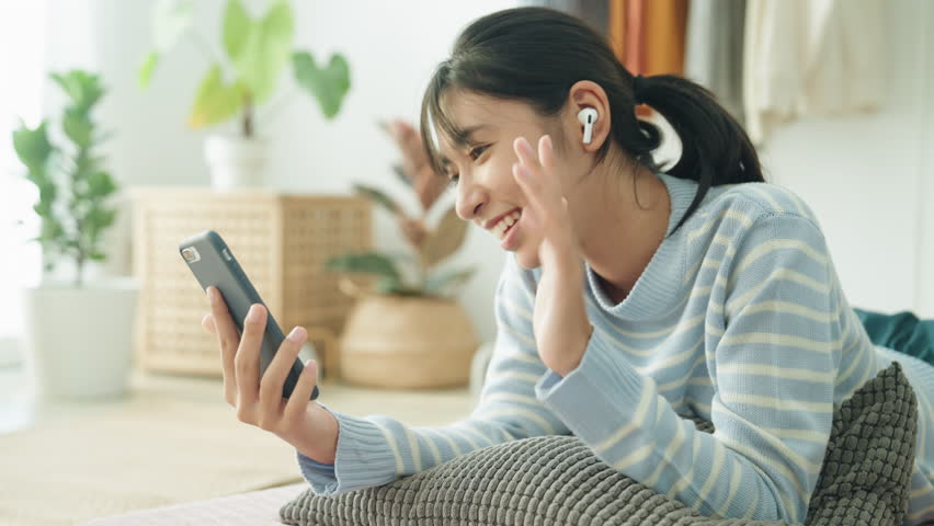 Asian teenager women using wireless headphones to make video calls and chat with friends in  bedroom happy.Asian teenager women are sleep and listen music.
