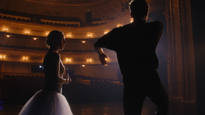 Graceful ballerina dances with partner in training suit and rehearses choreography moves on theater stage. Couple of ballet dancers practice before performance. Classical ballet art concept. Handheld. Royalty-Free Stock Footage #1102509459