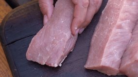 Closeup view 4k stock video footage of adult woman cutting piece of fresh uncooked organic pork meat at home using wooden board and small knife to chop it into small pieces