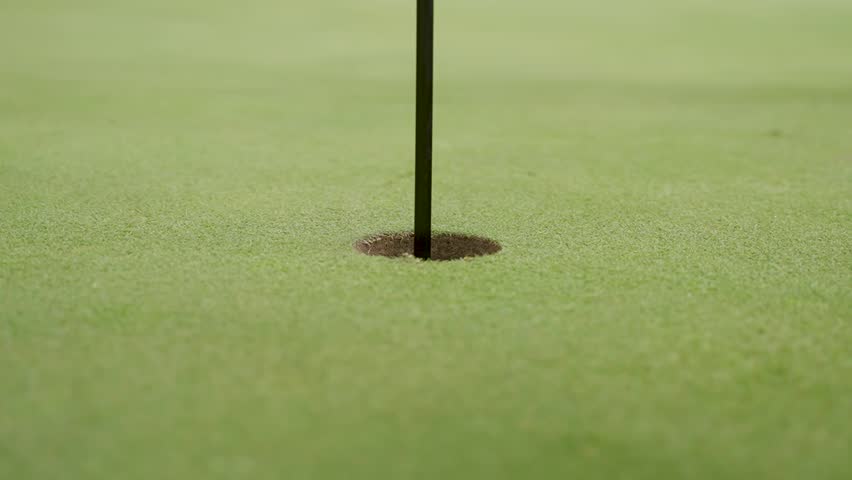 Slow motion shot of a golf ball rolling into a hole. Royalty-Free Stock Footage #1102511515