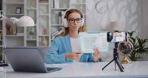 Woman making online presentation. Female business coach blogger filming educational workshop or lecture on mobile front camera at home, sitting at workplace table.