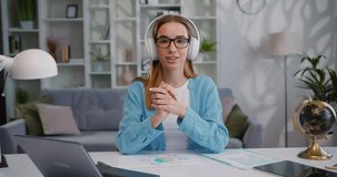 Blogger woman in headphones speaking at webcam, working, giving webinar, shooting video, recording podcast, making conference call at home office desk. Study vlog job.