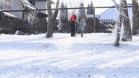 Laughing, active brunette long haired woman in winter clothes riding and wheeling little girl on sledge. in winter area in tree yard. Family activity and fun on holidays or on weekends. Video, 4k