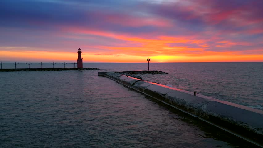 Iconic Lighthouse beacon silhouetted against fiery Lake Michigan twilight horizon, moving aerial view.