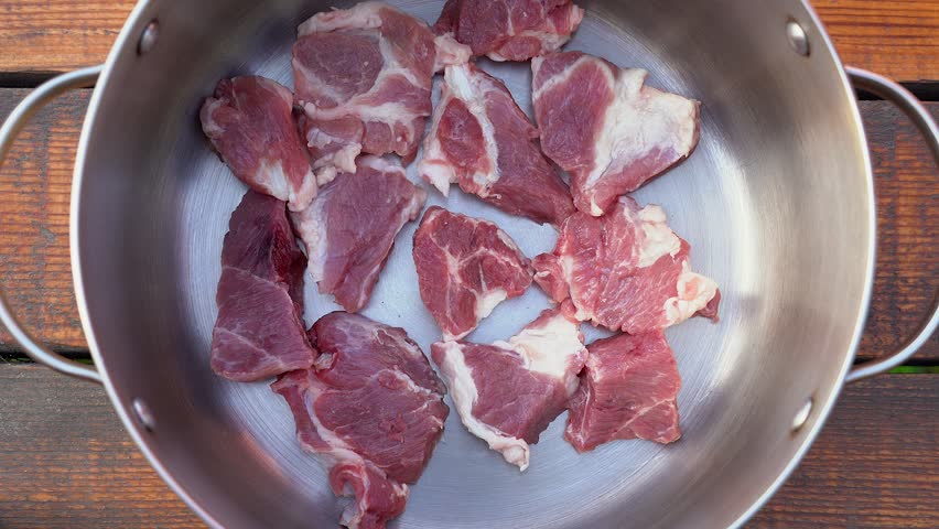 Closeup top view stock video footage of pieces of fresh uncooked pork meat ilaying on bottom inside of pot