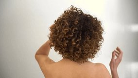 Rear view of female model, with curly afro hair, looking at the camera while playing with her hands on her head. Caucasian woman with bare shoulders - Powered by Shutterstock - Get 15% off with code: PIKWIZARD15