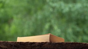 Closeup view 4k video of 4 stacked old paper books laying on wooden shelf outdoors isolated on green foliage bokeh background