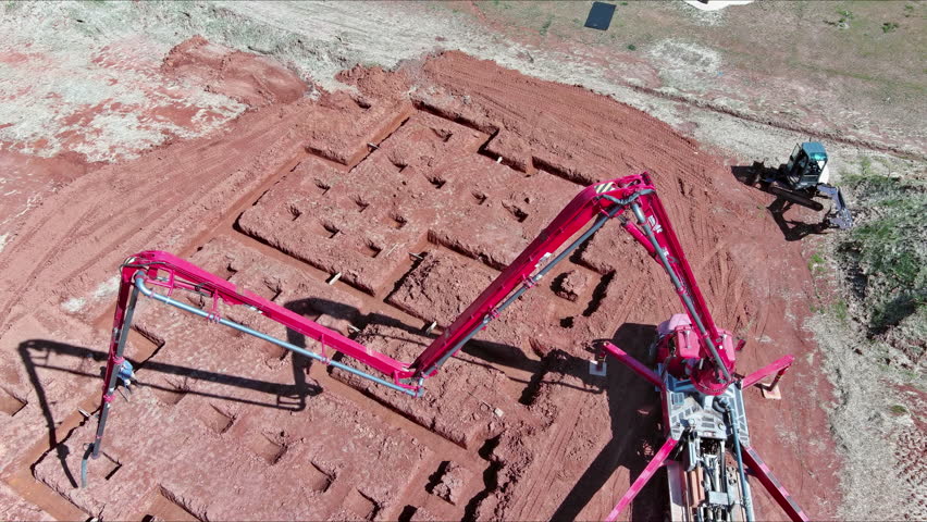 Concrete is poured for laying foundation of building by worker using an automatic pump to direct cement concrete