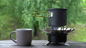 Making hot morning coffee or tea using travel equipment. Closeup view 4k video of small gas burner with cooking pot and boiling water inside of it