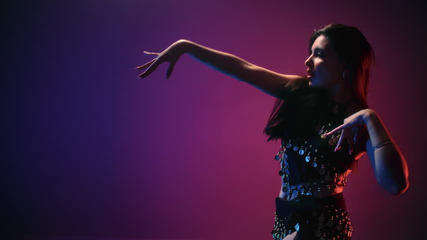 Sensual flex Asian woman belly dancer performance show elegant movement in traditional clothes neon ultraviolet studio. Female seductive dancing oriental ethnic costume with sequins jewelry side view