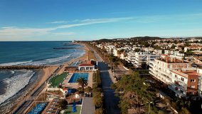 Drone flight back over in along coast beautiful beaches surrounded by Palm trees in Sitges. Mediterranean landscape of beach and hotels. Gentle sea waves quietly roll onto shore. Film intro. 4K video