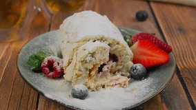 Tasting a slice of meringue roll cake with fresh berries. Woman cutting a piece of meringue roulette with fork, close up video clip, summer dessert served on plate. High quality slow motion 4k footage