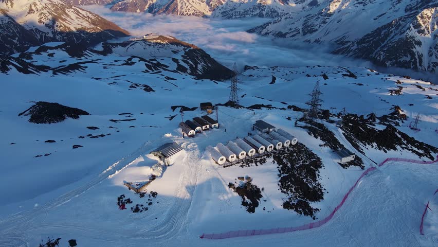 Aerial view of the mountain climber shelters on the slope of Mount Elbrus in the shape of huge barrels. A beautiful panorama of the mountains at sunset. Lodges for climbers while climbing the mountain