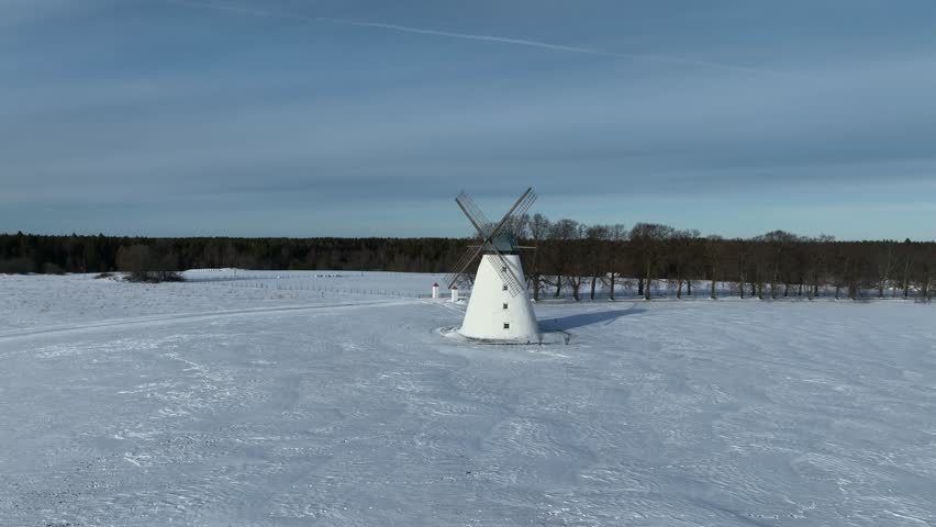 Rotating panoramic aerial view of Vihula windmill in winter with white snow covering the ground, Lahemaa, Estonia.