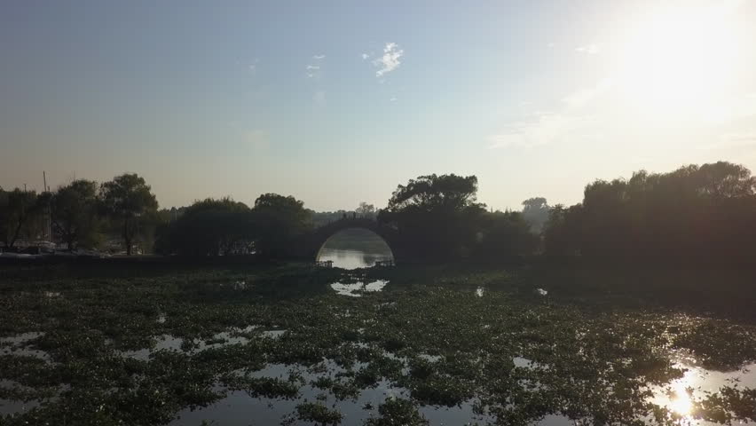 Beautiful aerial: Weed choked pond to ancient China stone arch bridge