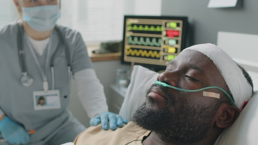Selective focus medium close-up of female doctor wearing mask checking health condition of African American patient with head injury Royalty-Free Stock Footage #1102542131