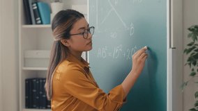 Asian woman teacher writing geometry equation on chalkboard, talking to students - Powered by Shutterstock - Get 15% off with code: PIKWIZARD15