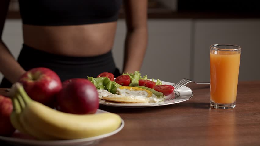 Cropped view of woman eating scrambled eggs with vegetables and drinking orange juice for breakfast