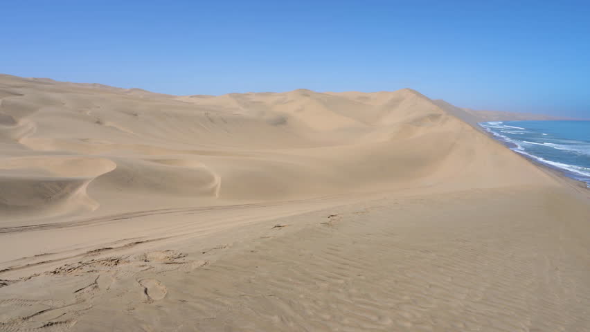 Pan on the Namib Desert meeting the Atlantic Ocean in the Skeleton Coast near Sandwich Harbour in Namibia, Africa. Royalty-Free Stock Footage #1102547327