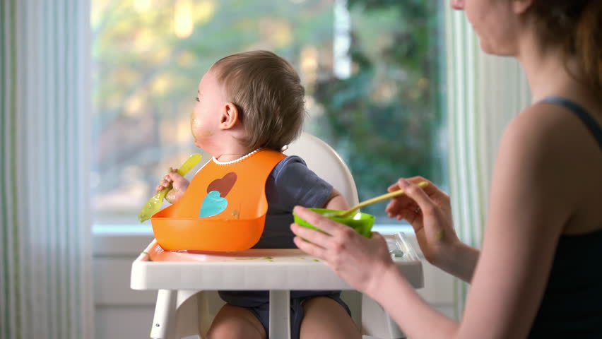 Mother feeding her baby son with fruit vegetable puree in baby chair. The baby crying and does not want to eat Royalty-Free Stock Footage #1102549375
