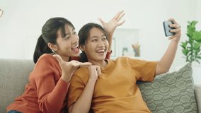 Asian female friend sit on the sofa together, using their 
smartphone take pictures, smiling and happy.
