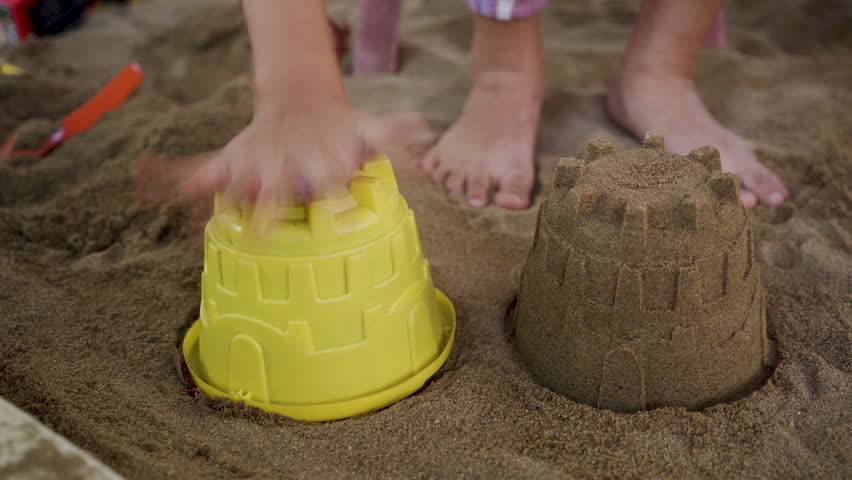 4K, Hand close-up little boy is playing in sand on beach is scooping sand into castle mold, In order build sand castle by sea from mold that must be tightly packed pour out get beautiful shape. Royalty-Free Stock Footage #1102557737