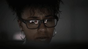 
Lateral Dolly of Young Focused African American Businesswoman in Eye Glasses Late at Night Working in Front of Computer. Several Animation Videos Reflected in Glasses. 