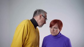 Old man whispering secret to his wife, something negative. Gray-haired man and red haired woman are standing isolated. Woman is dissatisfied. 4k video footage