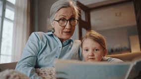 Slow motion Authentic portrait of 60 years old Caucasian elderly pretty woman, loving grandmother, wearing eyeglasses, enjoying wonderful moments with her little grandchild, reading fairy tales to her - Powered by Shutterstock - Get 15% off with code: PIKWIZARD15
