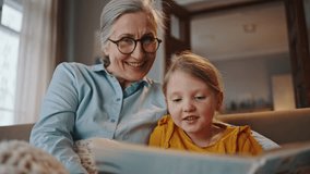 Slow motion. Adorable redhead little kid girl smiles, expressing happiness spending weekend with her loving grandmother at home, enjoying reading fairy tales together. Happy family relationships - Powered by Shutterstock - Get 15% off with code: PIKWIZARD15