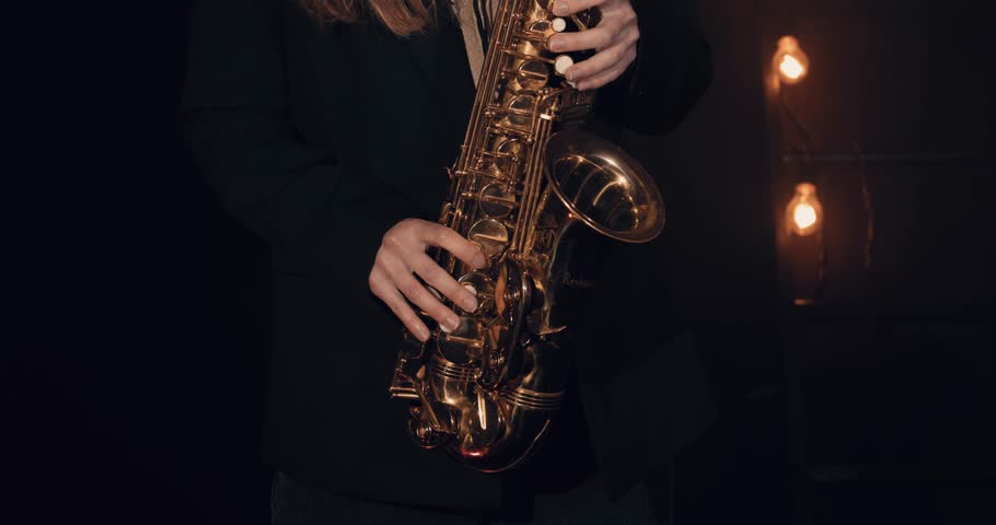 Young girl playing saxophone against a black background. Close-up. Several light bulbs in the background. Cinematic view