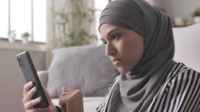 portrait of serious thoughtful muslim woman sitting on the floor using smart phone,side view of young arab female browsing on smartphone at home - Powered by Shutterstock - Get 15% off with code: PIKWIZARD15