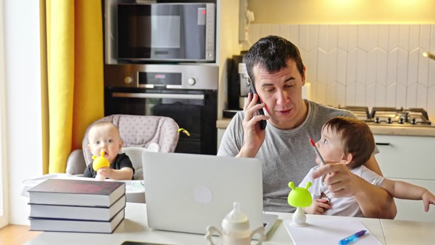 father working from home remotely with baby daughter in his arms. pandemic remote work business concept. father tries to work at home kitchen, baby children interfere sitting on their hands fun Royalty-Free Stock Footage #1102576977