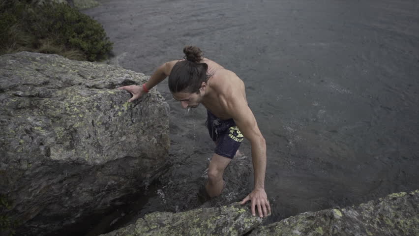 Man with a ponytail emerges from the water with muscles congested from the cold