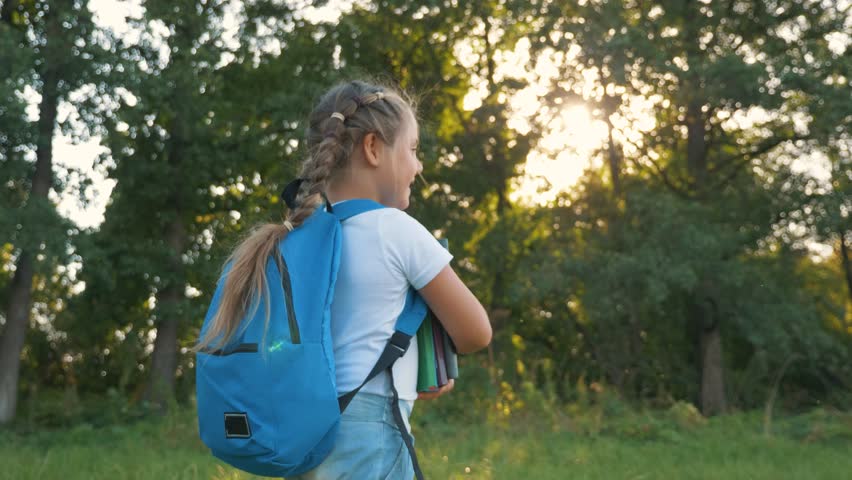 Back to school. cute happy girl with backpack walks through park to school with books in her hands. girl is holding textbooks in her hands. Walk on road to school. Walk in park to school. Royalty-Free Stock Footage #1102590897