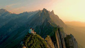 Couple at the hedge of a mountain watching the sunset, Schaeffler mountain ridge swiss Alpstein, Appenzell Switzerland, a steep ridge of the majestic Schaeffler peak during summer - Powered by Shutterstock - Get 15% off with code: PIKWIZARD15