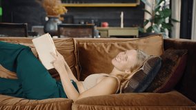 Happy positive young woman reading book on sofa at home and laughing. Girl flirting, coquet. Staying at home alone - Powered by Shutterstock - Get 15% off with code: PIKWIZARD15
