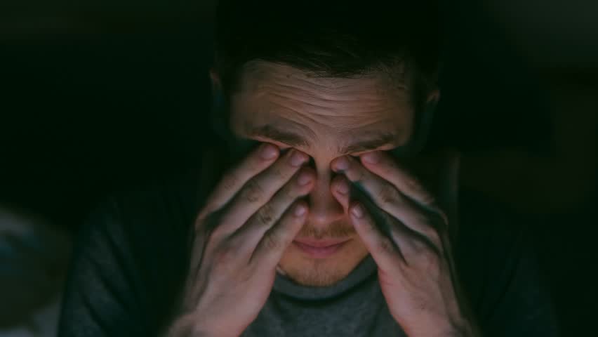 A young person is sitting at night at the TV, tired, watching the news, rubbing his eyes with fatigue. High quality 4k footage | Shutterstock HD Video #1102606627