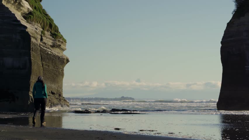 Woman walking by Three Sisters Beach with Mount Taranaki behind, New Zealand.