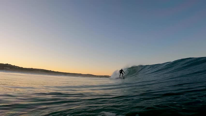 Close up, man surfs large wave at huge sunset in Cascais, Guincho, Abano.