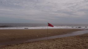 Aerial orbiting shot of red flag waving on sandy beach of Punta del Este during stormy day in Uruguay  - Powered by Shutterstock - Get 15% off with code: PIKWIZARD15