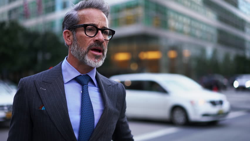 Adult Prosperous businessman in suit and stylish eye glasses stands on city street while talking to female colleague. Business people discussing something while standing on busy street. Communication  Royalty-Free Stock Footage #1102615855