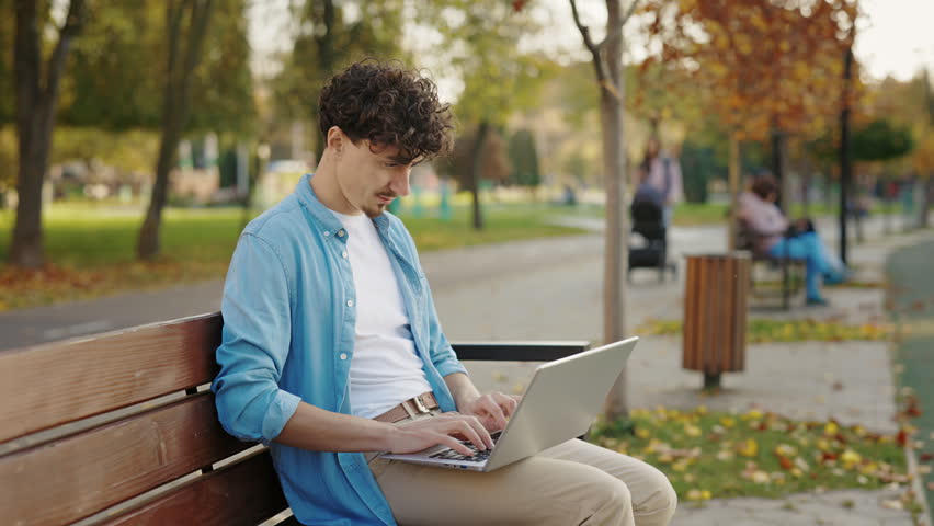 Bearded Man Sitting on the Bench in the Street, Using his Laptop. Caucasian Male It Worker Outside Working on the Computer in the Park. Student Distant Studying Outdoor