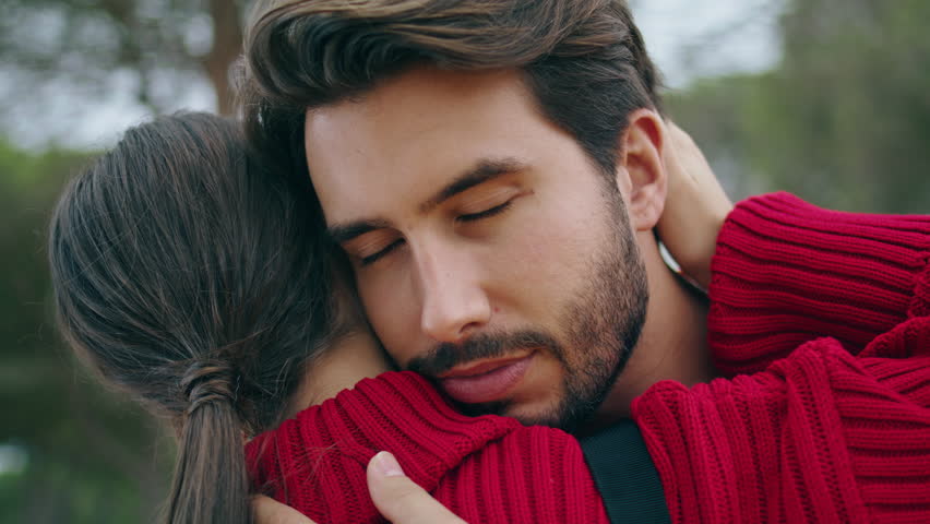 Closeup handsome bearded man hugging young woman on nature. Attractive guy embracing lovely girl outdoors looking camera. Happy couple feeling love tenderness enjoy romantic date. Relationship concept