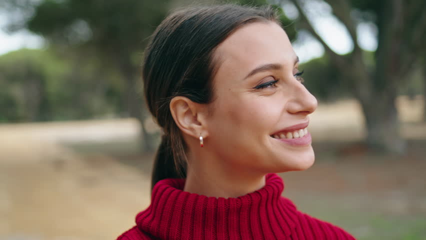 Joyful cheerful girl laughing happily standing on nature wearing red sweater close up. Portrait of attractive happy woman having fun in beautiful park. Smiling carefree brunette enjoy weekend outdoors