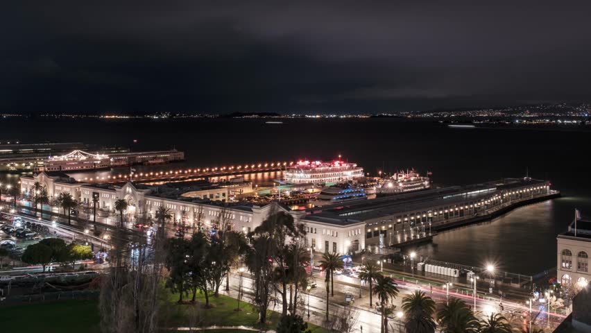 San Francisco, USA - December 31st 2022: Night time time lapse of cars passing along the Embarcardero in San Fransisco as people and boats collect around the harbour to watch the firework display