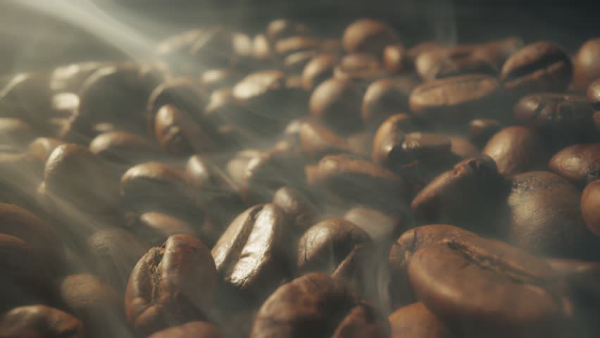 Slider shot of coffee beans during roasting. Dark roasted coffee beans with smoke. Smoke comes from fresh coffee seeds. Macro shot, 4K